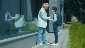 A young boy begins his school day, walking confidently toward the entrance while waving back at his kneeling mom. A common but heartfelt moment in a modern setting. - Powered by Shutterstock - Get 15% off with code: PIKWIZARD15