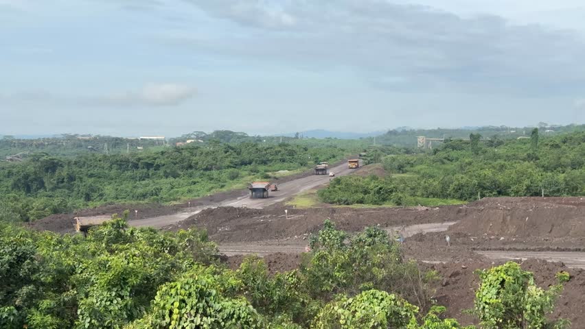 Industrial activity is apparent in this landscape featuring heavy machinery used for hauling minerals along a road, depicting mining operations and environmental impact.