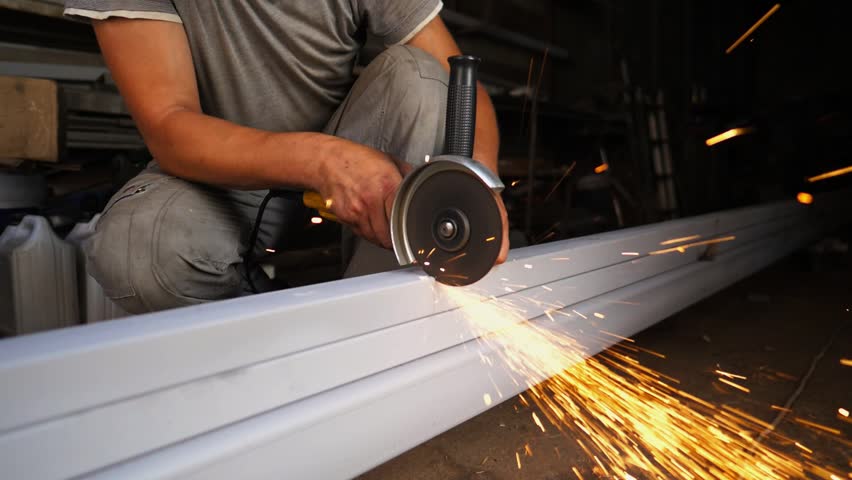 Arms of professional repairman sawing metal construction with a circular saw at garage. Male hands of young craftsman cuts iron using electric grind wheel at workshop. Close up Slow motion