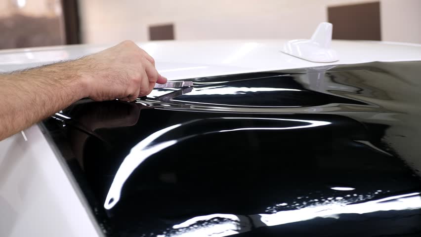 A close-up of the car servicemaster glues the tinting film on the glass, he smoothes the foil with a spatula. The process of tinting a car in a car service.