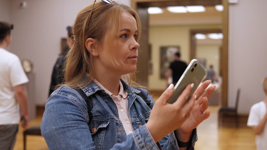 Close-up portrait of a woman with a phone in an art gallery. A family of tourists visits an art gallery and takes pictures on their phone.