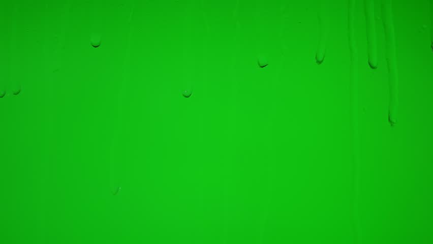 Close up of wet glass with dripping water drops and streaks of rain, on a bright green chroma key background, perfect for visual effects and background replacement.