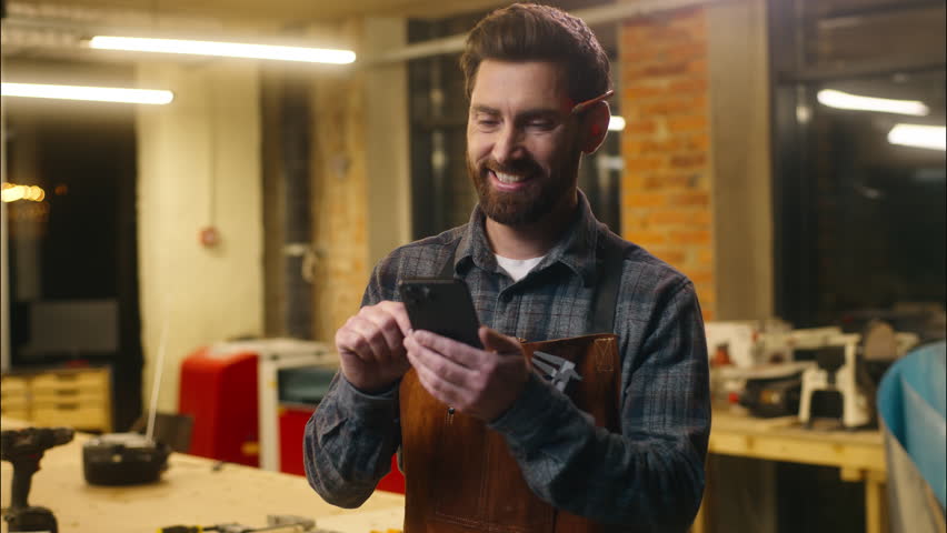 Happy Caucasian man carpenter using mobile phone in workshop wood master craftsman swiping screen device smiling artist male architect order hardwood online shopping guy browse app Internet carpentry