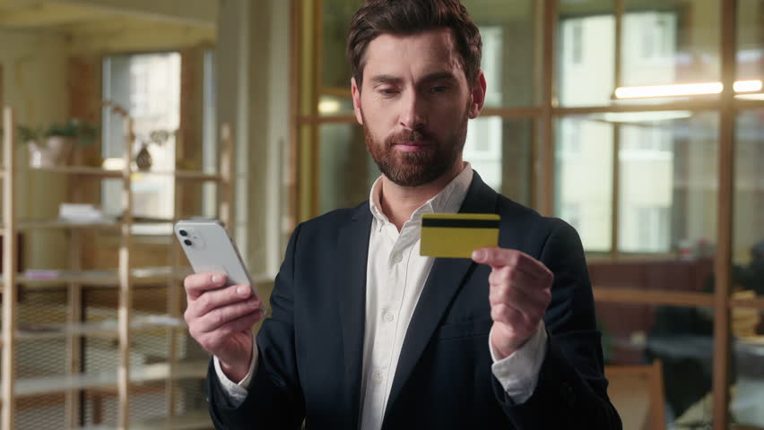 Business smiling Caucasian man paying credit card using mobile phone in office male manager entrepreneur buyer banking app guy ceo leader cashless payment businessman buying online e-commerce finance