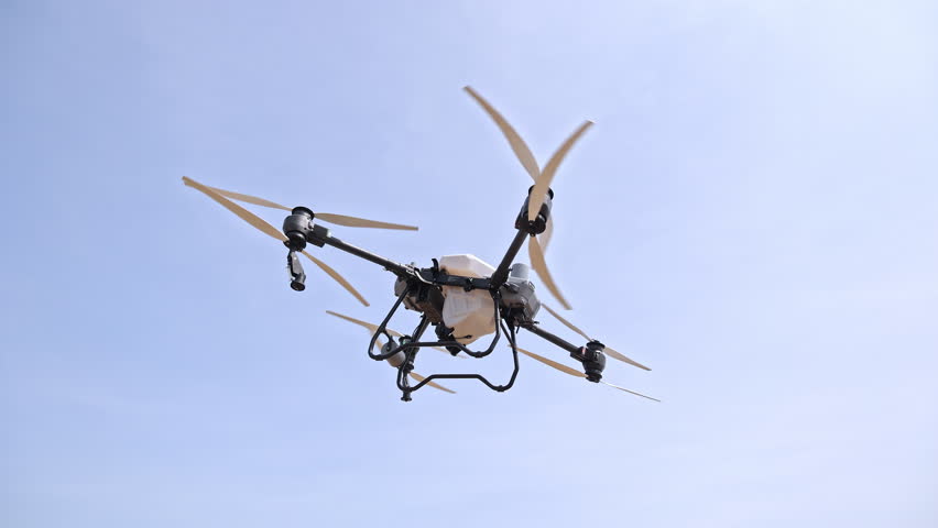 Close-Up of Flying Agricultural Drone, High-Tech Farming Equipment Operating Against Blue Sky Background