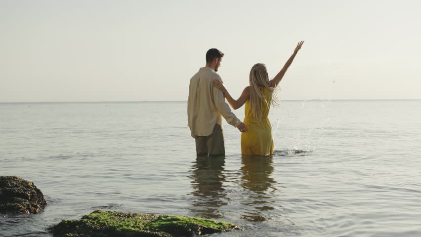Couple enjoys playful moments together in shallow water during sunset at a serene beach location