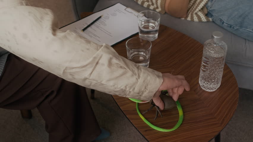 High angle shot of female patient in VR headset with arachnophobia touching fake spider during individual therapy session lying on couch and sharing emotions with unrecognizable psychologist