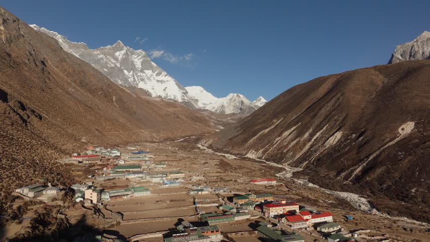 Aerial view of a remote village in the center of mountains of Nepal, showcasing traditional architecture and a majestic snow-capped peak in the background