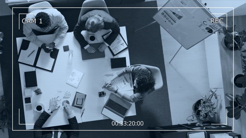 High angle surveillance camera shot of professional team of four diverse young business analysts having discussion sitting together at white table in office setting