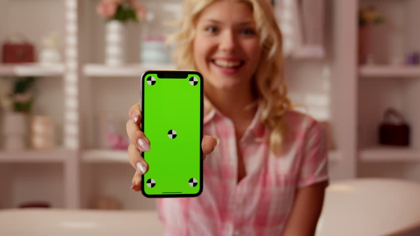 Portrait Caucasian teen girl teenager woman female showing green screen mobile phone excited in candy pink bathroom smiling looking at camera happy positive holding smartphone with chroma key display