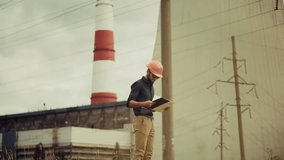 Engineer in hard hat reviewing construction plans at industrial site with power plant in background. Energy infrastructure, field inspection, and engineering development in progress. Industrial site - Powered by Shutterstock - Get 15% off with code: PIKWIZARD15