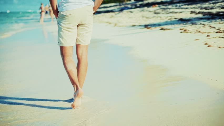 relaxing on tropical beach resort.  walks barefoot along shallow edge of pristine beach gentle waves lapping at their feet. Feelings of summer vacation, relaxation, seaside tranquility. Beach walk