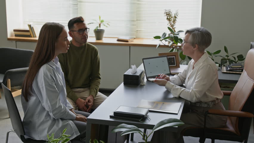 Female therapist conducting associative exercise with cards working with adult biracial couple during family psychotherapy session while sitting at desk in modern office