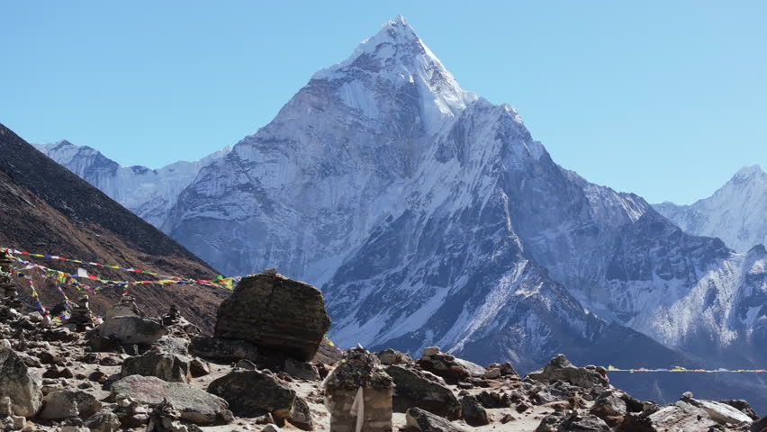 A breathtaking view of a snow-capped mountain in Nepal, adorned with colorful prayer flags, under a clear blue sky