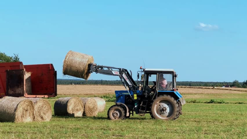 tractor loading hay bales in a truck across a vast field on summer day