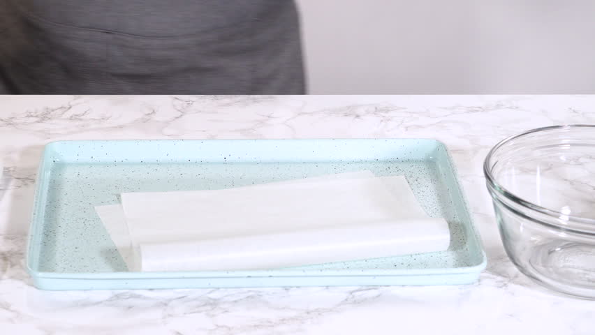 A light blue baking dish is shown with parchment paper laid flat inside it. Simple, clean visuals suited for baking demos, prep sequences, or food channel intros.
