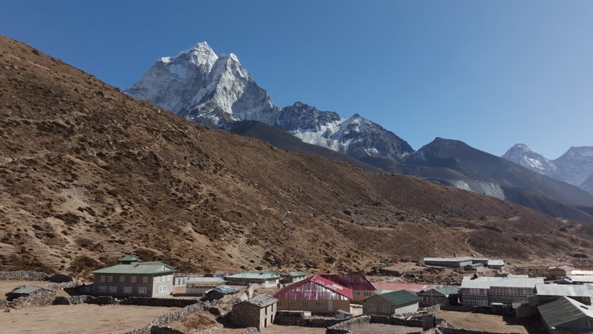Skyward view of a hidden Nepali village in the mountains, featuring wooden-roofed homes and stately snowy peaks