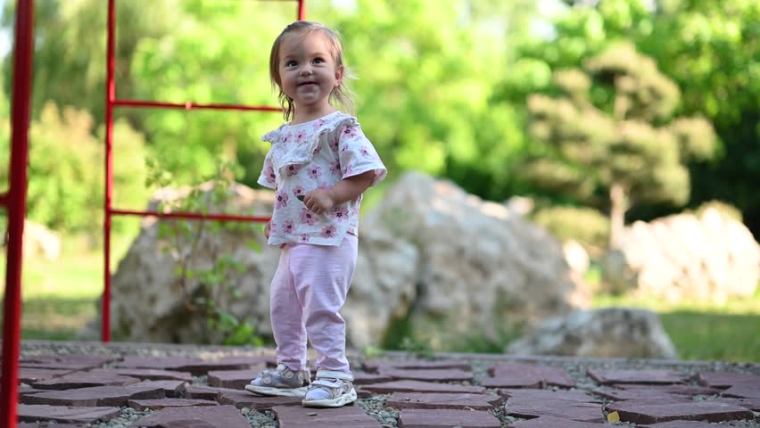 A Happy Little Girl is Walking on a Stone Path in a Beautiful Summer Garden.