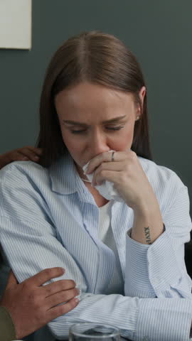 Vertical shot of crying woman talking to compassionate male spouse at counselling office while female psychotherapist noting on emotional interaction between couple