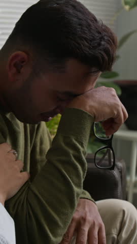Vertical shot of female partner consoling frustrated Indian man crying during family counselling session in therapists office