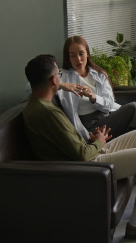 Vertical zoom shot of focused middle aged female psychotherapist writing in notebook listening to partners emotional discussion during couple therapy session in office