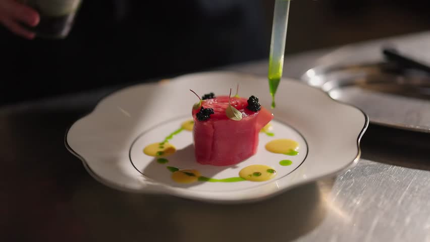 A pastry chef's hand decorating a gourmet dessert plate with a pink sauce from a squeeze bottle