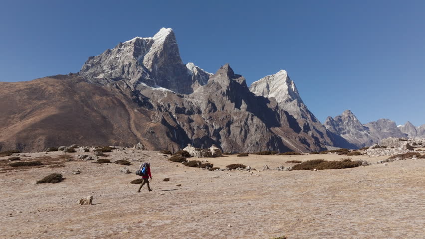 Hiker Trekking Across a Rocky Plain in the Himalayas of Nepal, with Majestic Snow-Capped Mountains in the Background