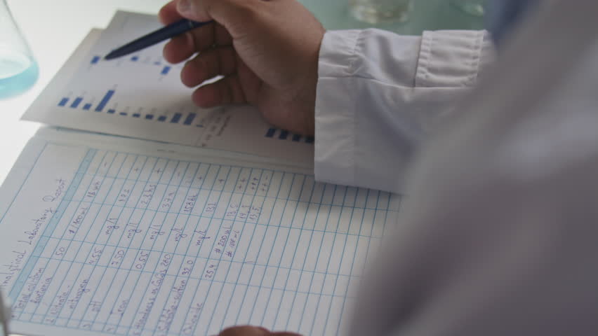 Hands of unrecognizable male scientist analyzing bar charts and taking notes on laboratory report during research work. Close-up view