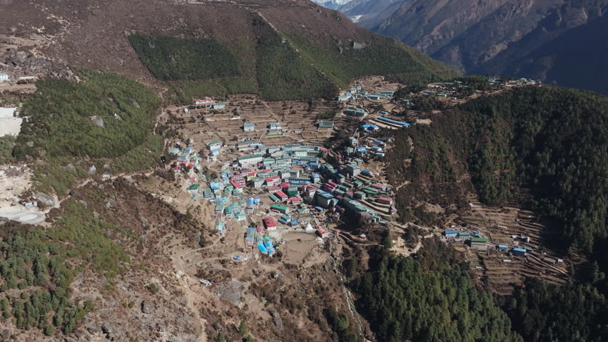 Aerial view of a far away village nestled in the mountains of Nepal, showcasing traditional architecture and a majestic snow-capped peak in the background