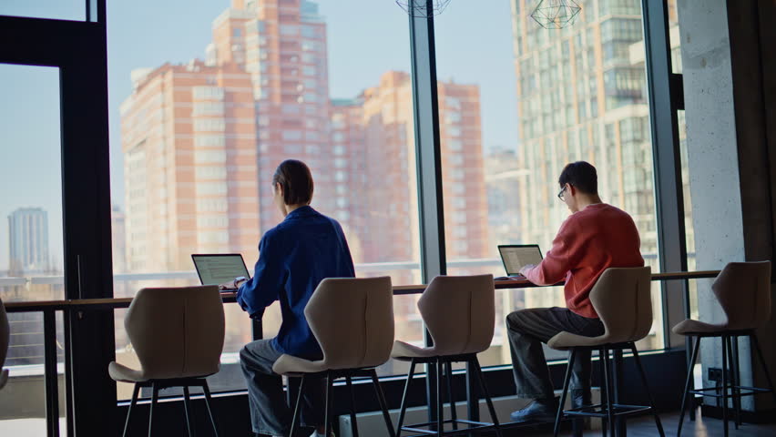 Colleagues busy of online work at contemporary workspace. Two freelancers focused on laptops creating project together at coworking space. Hardworking man manager asking advice in professional woman.