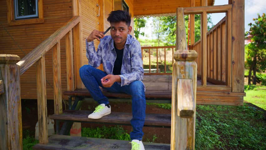 Explorer sits on timber stairs chatting by mobile outdoor, Holidaymaker lounges outside discussing over device, Traveler enjoys fresh air during long chat, Young Man Atop Cabin Steps Making Phone Call