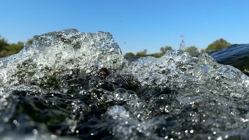Air bubbles fly along with the fast current of mountain river among smooth lines of algae among clear water. Underwater world of mountain river