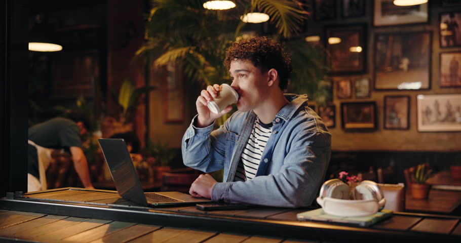 Coffee shop, hybrid work and man typing on laptop to research story or review email for journalism. Computer, drink and freelancer in cafe for news article, editing headline or fact checking at night