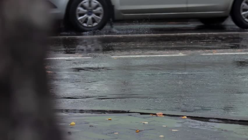 splashes from car wheels on the road while driving through puddles in the city after a hurricane in the fall. Cloudy weather, rainy season, flood on the road. Slow motion