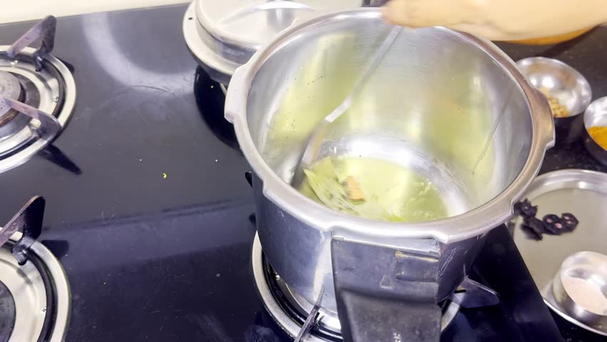 Aromatic Herbs Simmering in Kitchen Pressure Cooker, Bay leaves and spices crackle gently inside hot oil, Hand Stir Spatula flavorful mix ins over shimmering butter, Element pop audibly as heat builds