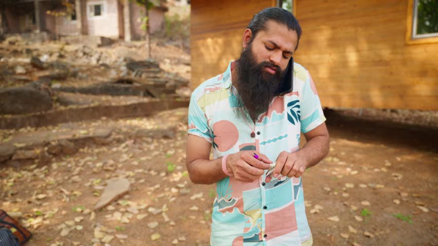 Bearded man holds phone while standing on leafy trail, He lights cigarette but stops midway with frown, Angry expression grows as he listens to caller, Male start shouting over smartphone, Countryside - Powered by Shutterstock - Get 15% off with code: PIKWIZARD15