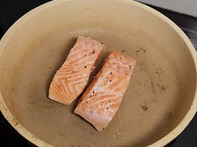 two pieces of salmon fillet being cooked in a pan