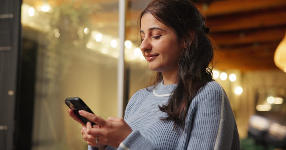 Phone, smile and woman in home at night for text, romantic message and internet notification. Mobile, person and communication for social media, chat and download app for online dating with bokeh