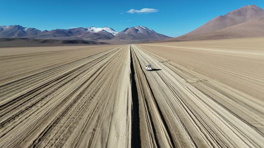 A drone view of a car driving across a desert under a blue sky in Bolivia. High quality 4k footage