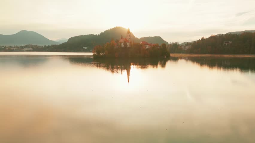 Aerial view of Lake Bled at sunrise in autumn, Slovenia. Scenic landscape with Pilgrimage Church on the island and medieval Bled Castle on a cliff above the picturesque lake surrounded by mountains.