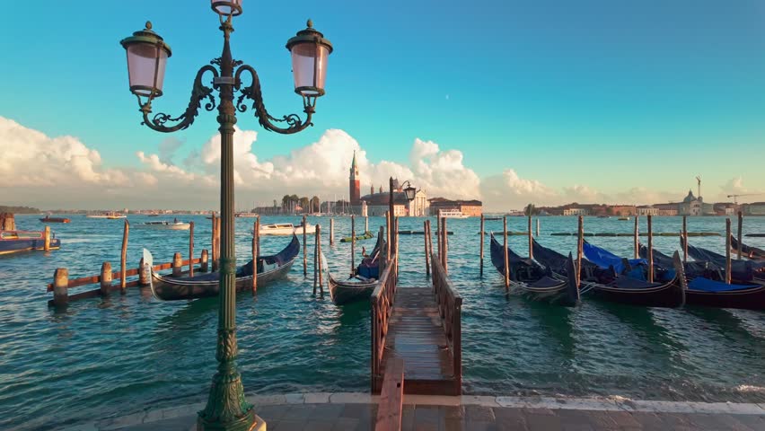 Iconic view of San Giorgio Maggiore church and traditional Venetian gondolas gently swaying on the water at sunset in Venice, Italy. Slow motion revealing footage