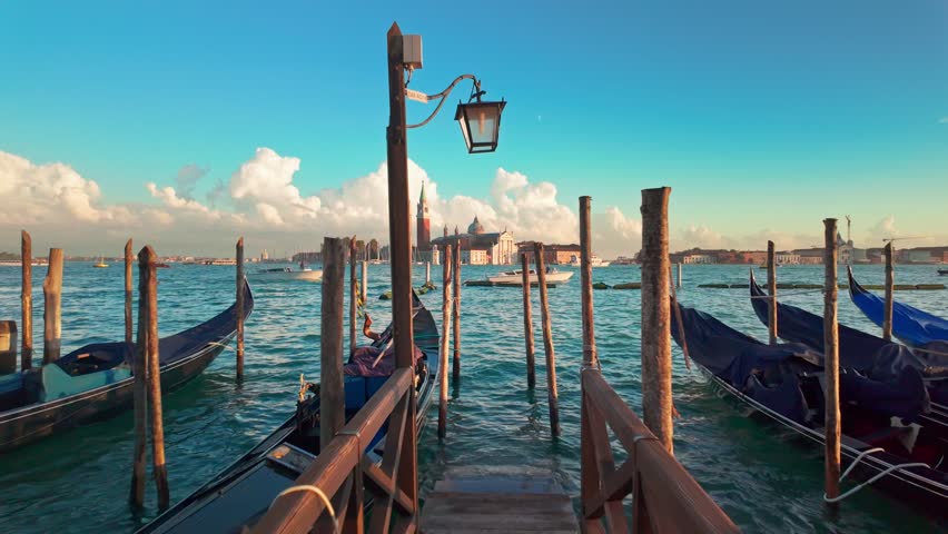 Iconic view of San Giorgio Maggiore church and traditional Venetian gondolas gently swaying on the water at sunset in Venice, Italy. Slow motion revealing footage