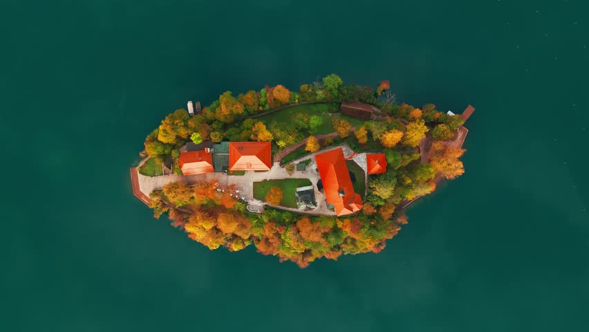 Aerial view of Lake Bled at sunrise in autumn, Slovenia. Top-down scenic landscape with the Pilgrimage Church on the island, surrounded by calm waters and vibrant autumn colors of the picturesque lake