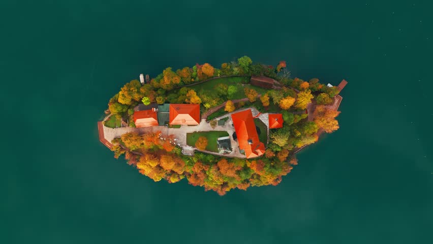 Aerial view of Lake Bled at sunrise in autumn, Slovenia. Top-down scenic landscape with the Pilgrimage Church on the island, surrounded by calm waters and vibrant autumn colors of the picturesque lake