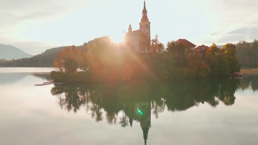 Aerial view of Lake Bled at sunrise in autumn, Slovenia. Scenic landscape with Pilgrimage Church on the island and medieval Bled Castle on a cliff above the picturesque lake surrounded by mountains.
