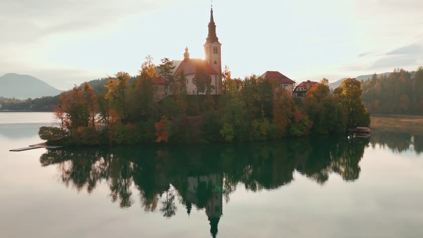 Aerial view of Lake Bled at sunrise in autumn, Slovenia. Scenic landscape with Pilgrimage Church on the island and medieval Bled Castle on a cliff above the picturesque lake surrounded by mountains.