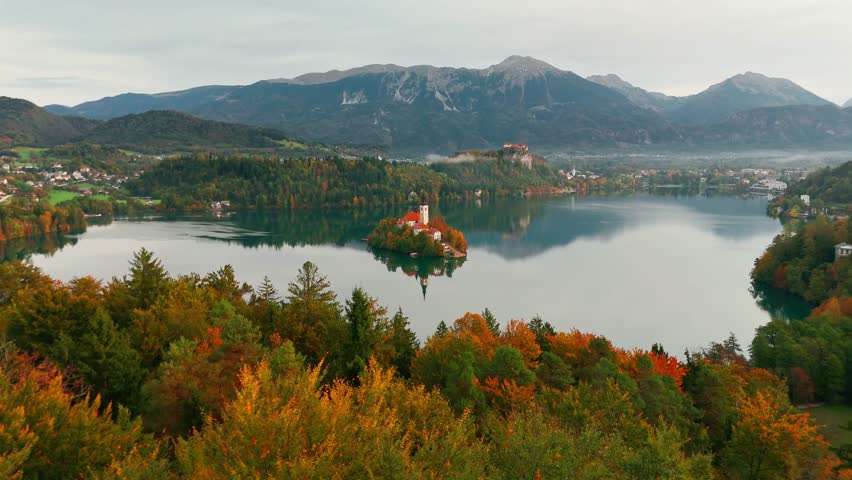 Aerial view of Lake Bled at sunrise in autumn, Slovenia. Scenic landscape with Pilgrimage Church on the island and medieval Bled Castle on a cliff above the picturesque lake surrounded by mountains.