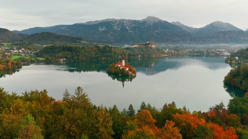 Aerial view of Lake Bled at sunrise in autumn, Slovenia. Scenic landscape with Pilgrimage Church on the island and medieval Bled Castle on a cliff above the picturesque lake surrounded by mountains.
