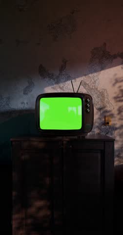 Retro TV in a dim room with chroma key screen - vertical video for social media purposes. Thunderstorm flashes cast shadows on textured walls. Halloween horror atmosphere. Clip seamless looped. CGI