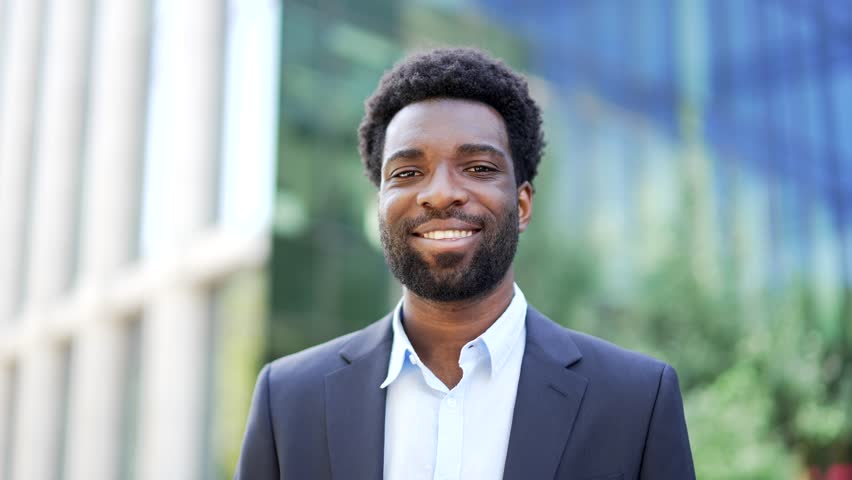 Portrait of smiling african american businessman in formal suit standing on street near office building. Happy male entrepreneur looking at camera. Head shot confident manager posing outside. Close up